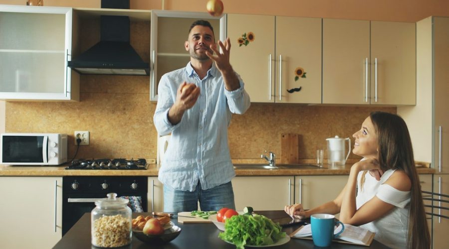 Attractive loving couple having fun in the kitchen. Handsome man juggle with apples to impress his girlfriend at home