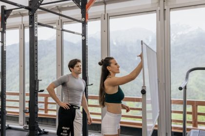 A gym coach instructs on whiteboard beside fitness equipment with mountain view.